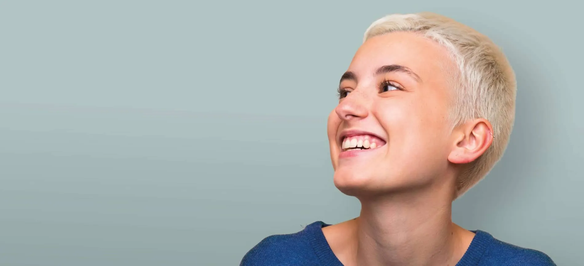 Junge, lächelnde Person mit kurzem, blondem Haar blickt motiviert nach rechts vor hellblauem Hintergrund.