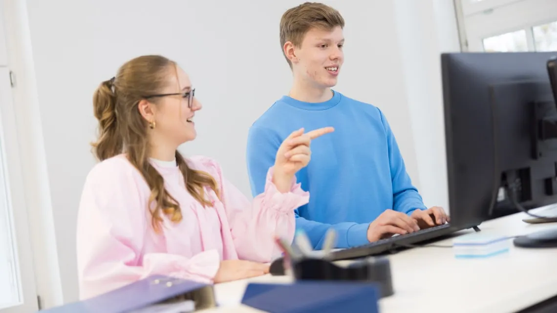 Zwei junge Kolleg:innen arbeiten gemeinsam am Computer im modernen Büro bei Westfalen Weser Netz.