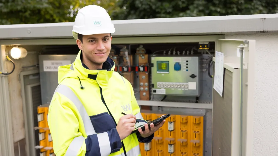 Junger Techniker prüft einen Stromverteilerkasten bei Westfalen Weser Netz und macht Notizen auf einem Tablet.