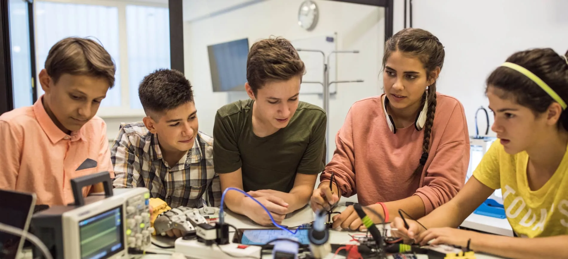 Fünf Jugendliche tüfteln gemeinsam an einem technischen Projekt mit Elektronik im Ausbildungsraum.