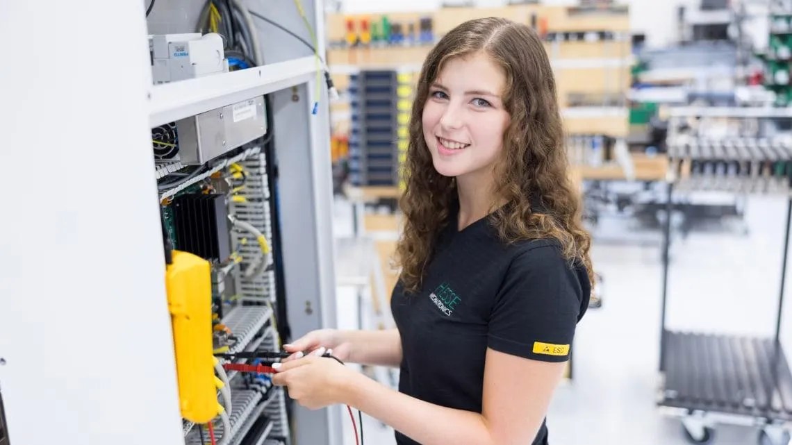 Junge Frau arbeitet lächelnd an einem Schaltschrank in einem modernen Technikraum bei Westfalen Weser Netz.