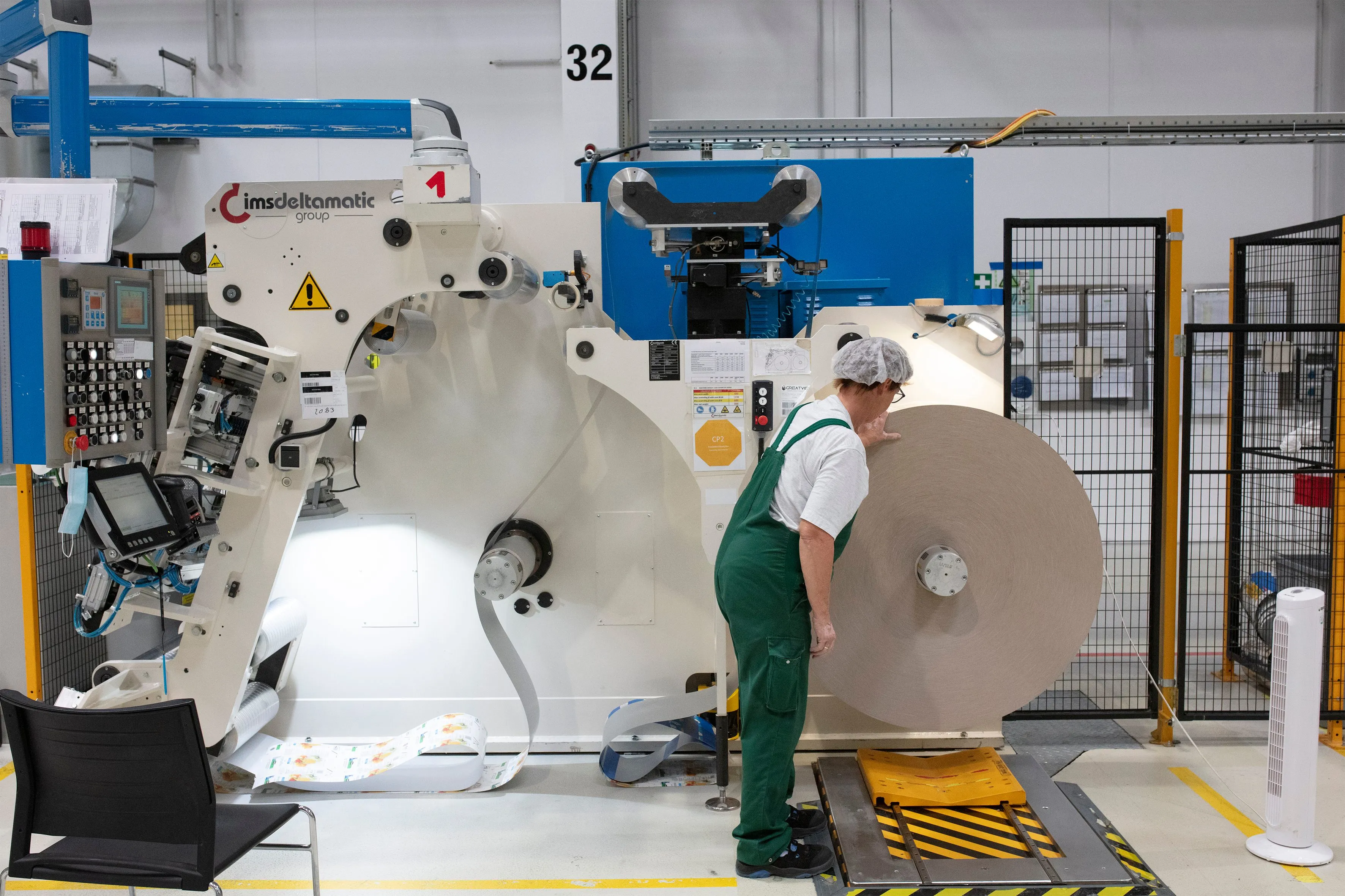 Ein Produktionsmitarbeiterin bei Wintipak bedient eine große Papiermaschine in einer Fabrikumgebung.