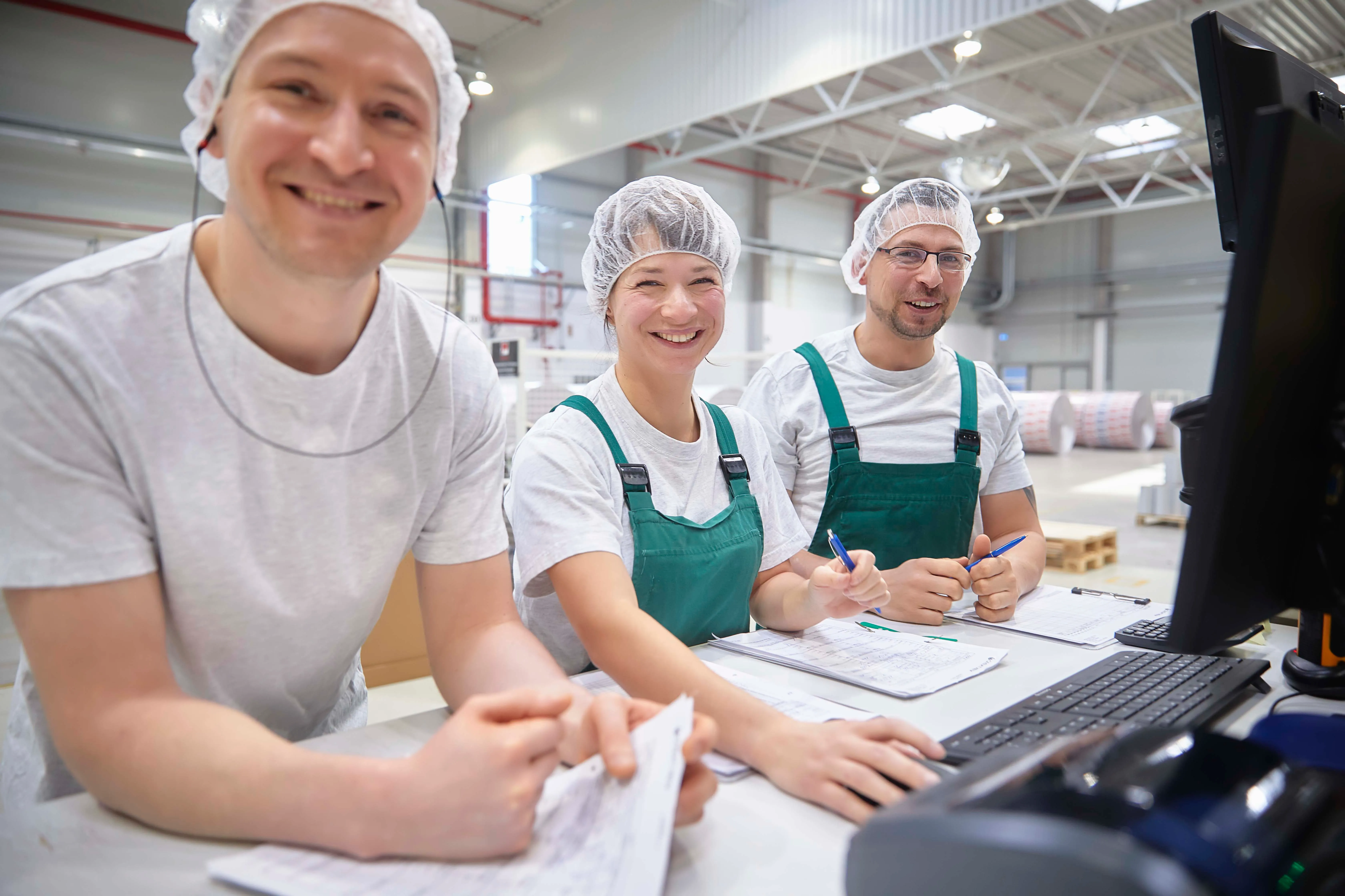 Zwei Mitarbeiter in grünen Overalls bewegen eine große Papierrolle in einer Produktionshalle bei Wintipak.