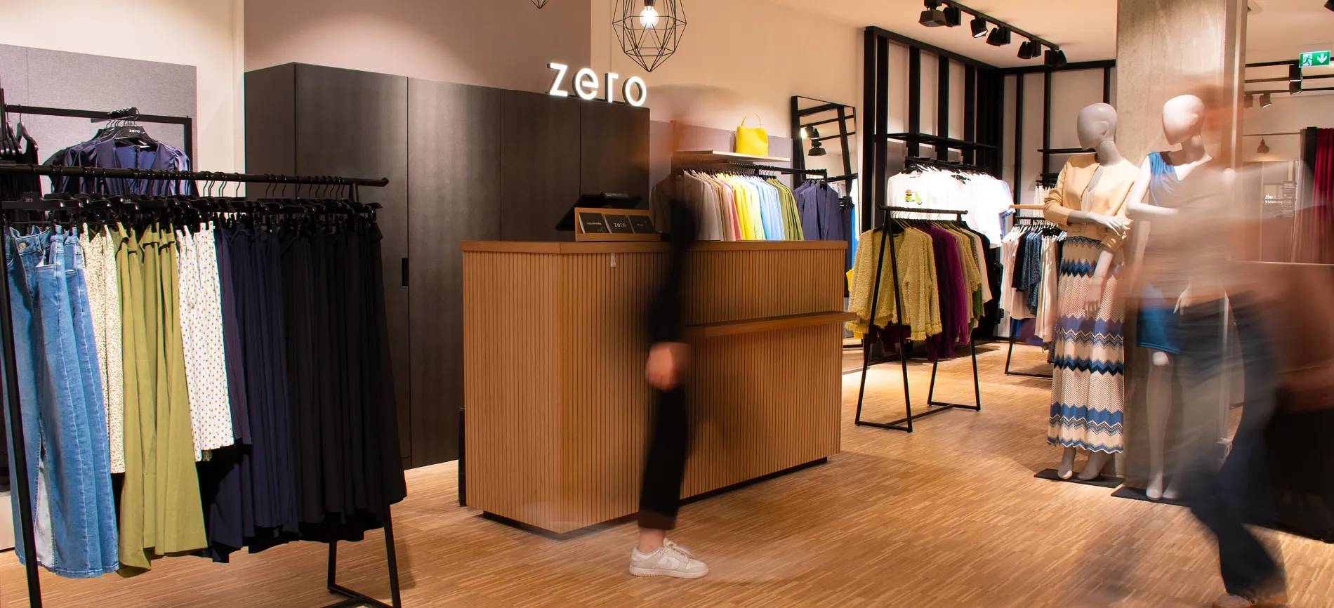 Mehrere schwarze Kleiderbügel mit Zero-Logo und Jeans in einer Ladenumgebung, die auf deinen Einstieg im Einzelhandel einlädt.