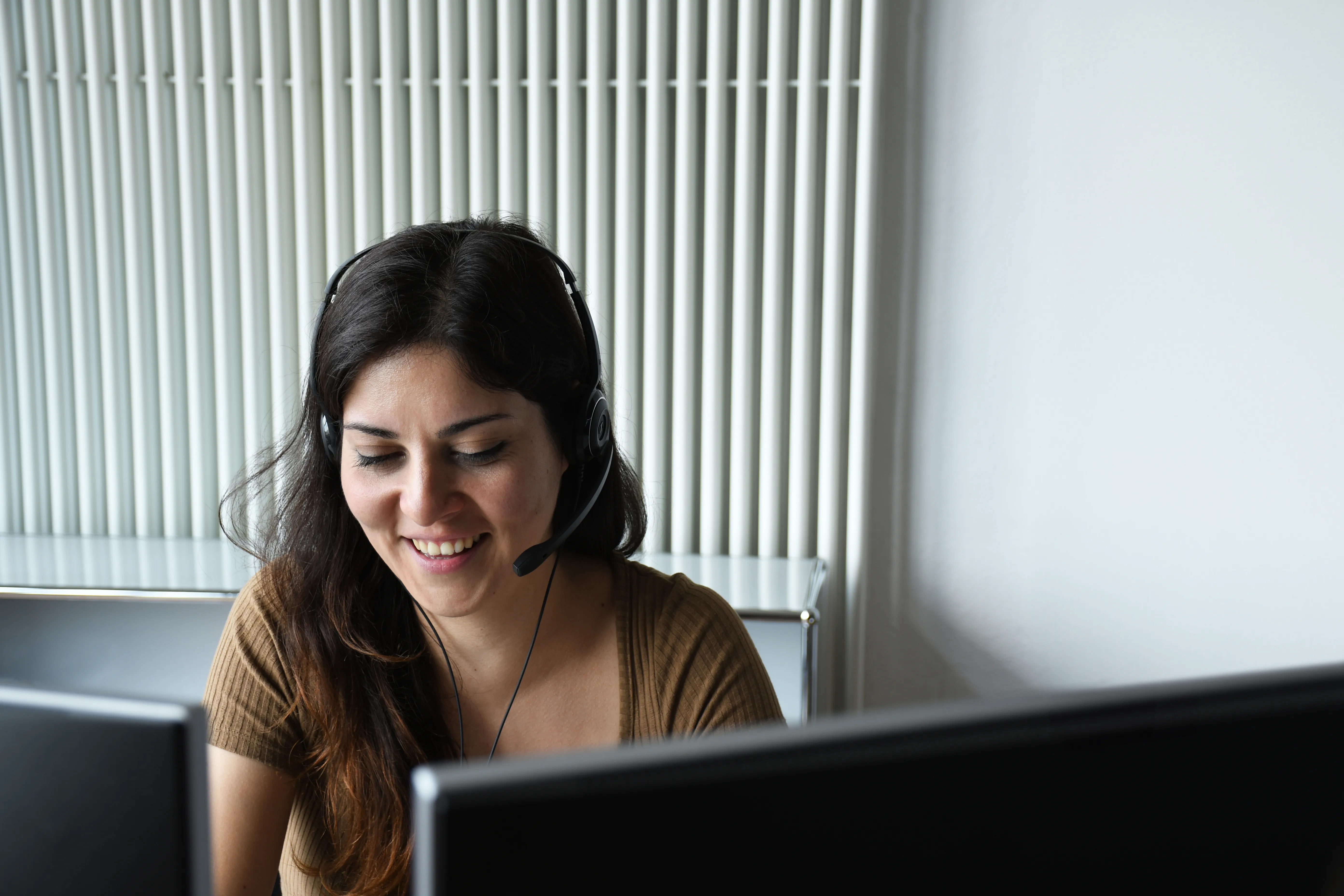Eine lächelnde Frau mit Headset arbeitet an einem Computer, ideal für Kundenservice-Jobs im Einzelhandel bei Zero | zPDC GmbH.