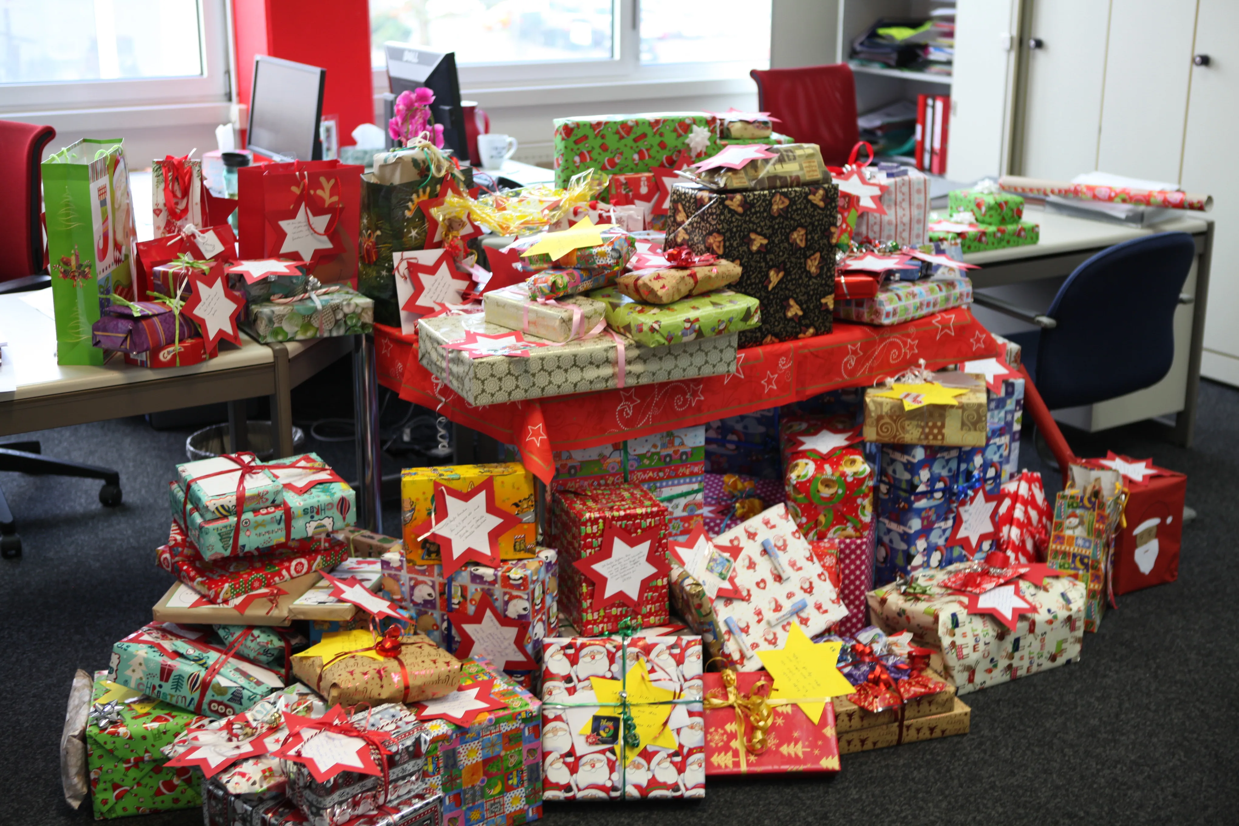 Viele bunte Weihnachtsgeschenke mit Sternkarten stapeln sich im ZF-Büro – hier erlebst Du Teamgeist und soziales Engagement.