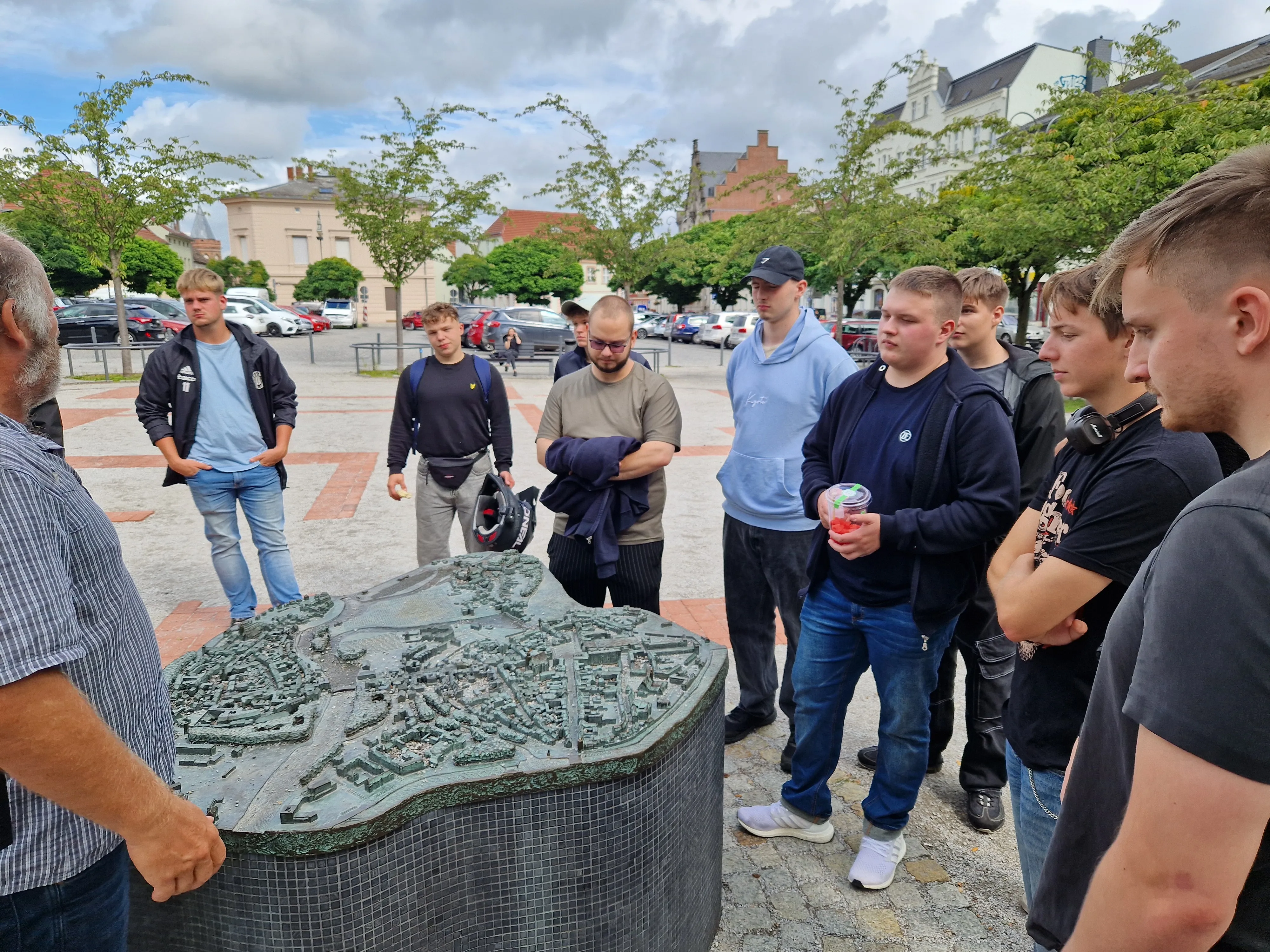 Eine Gruppe junger Menschen besichtigt gemeinsam ein Stadtmodell im Freien während einer Exkursion.