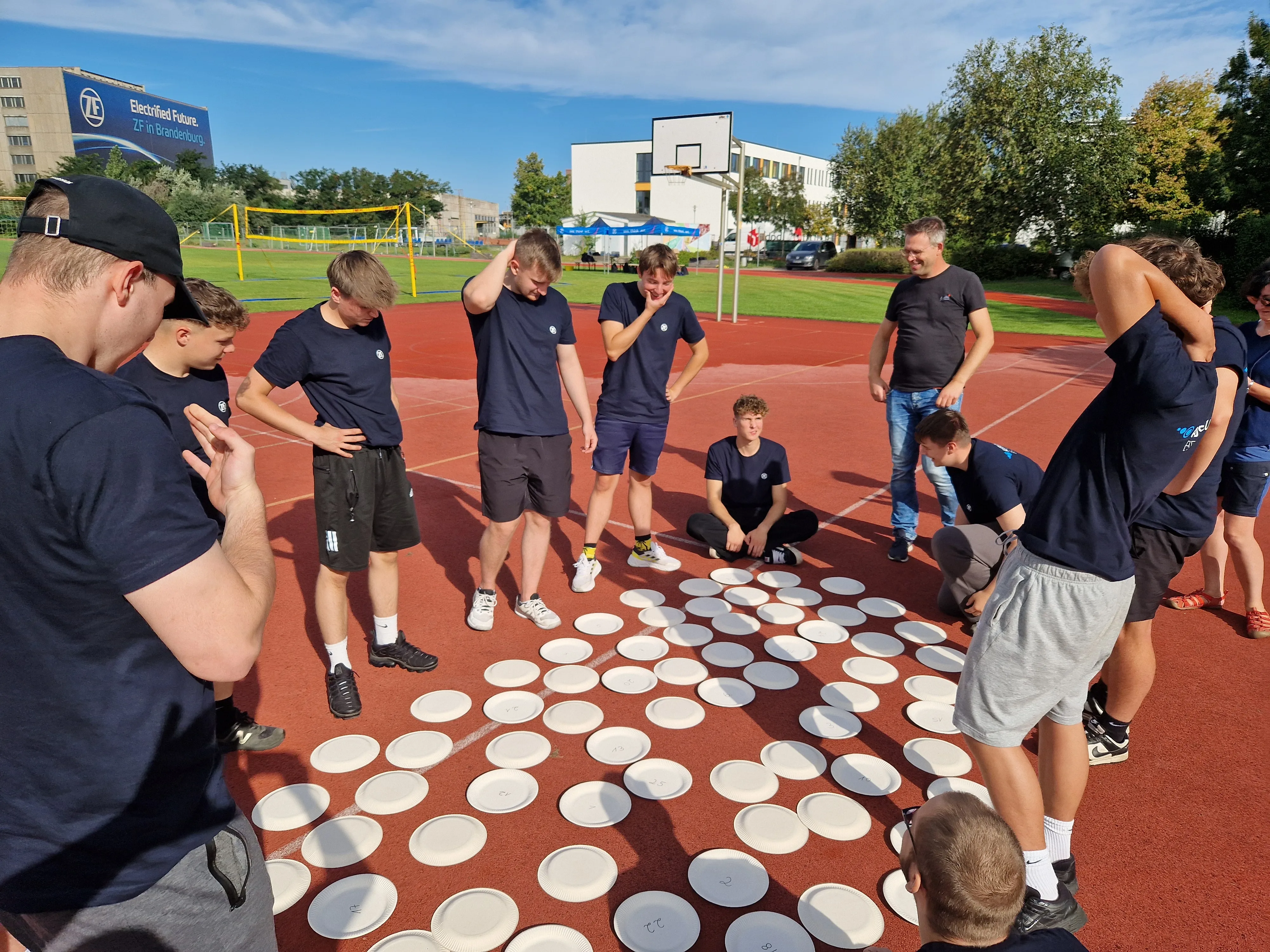 Junge ZF-Mitarbeitende lösen gemeinsam eine Teamaufgabe auf dem Sportplatz während eines Azubi-Events.