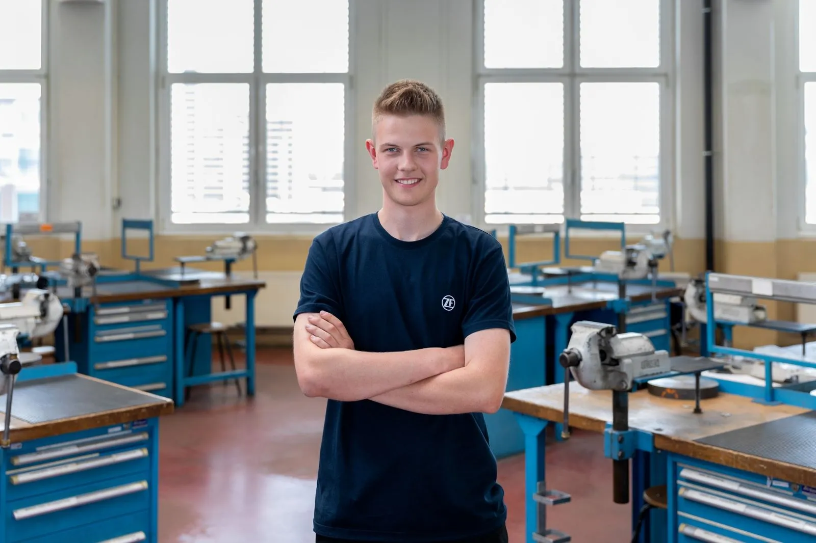 Junger Auszubildender bei ZF steht mit verschränkten Armen in einer modernen Ausbildungswerkstatt.