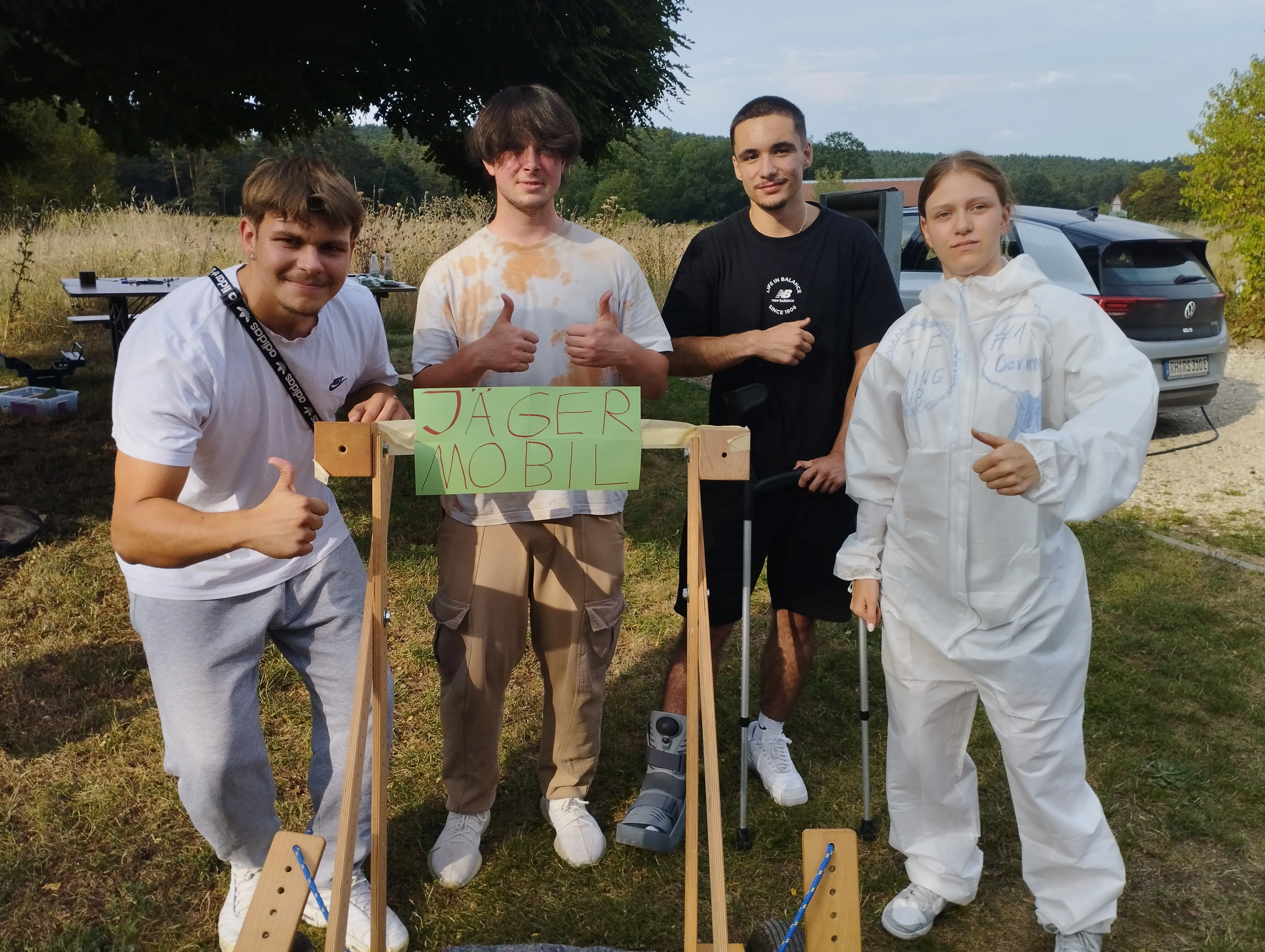 Vier junge Menschen präsentieren stolz ihr selbstgebautes „Jäger-Mobil“ und zeigen Daumen hoch beim ZF Team-Event.
